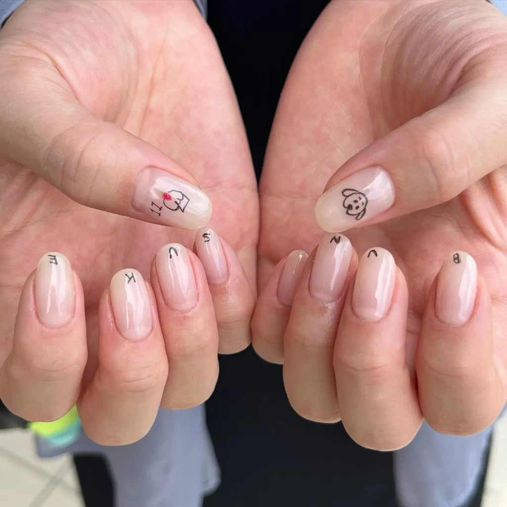 Cute short neutral nails with black letters and tiny drawings on clear base