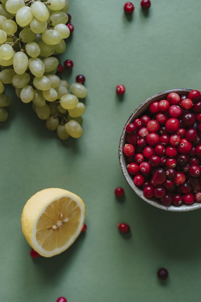 A flat lay of vibrant cranberries, grapes, and lemon on a green background.