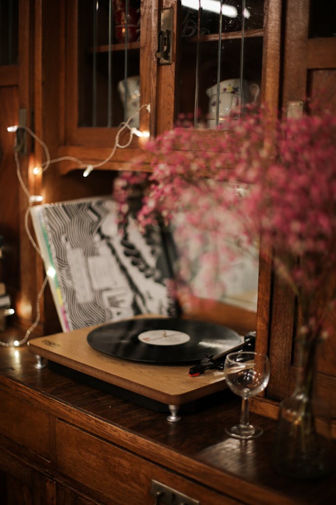 A vinyl record player on a wooden cabinet with flowers and fairy lights.