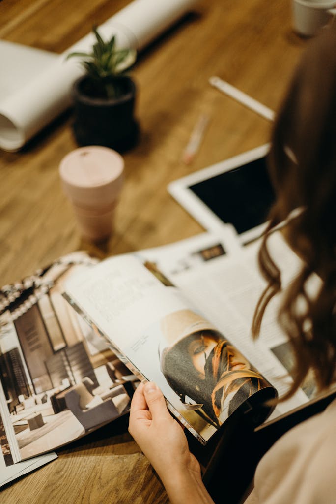 A woman engaging in reading a magazine at a wooden table indoors.