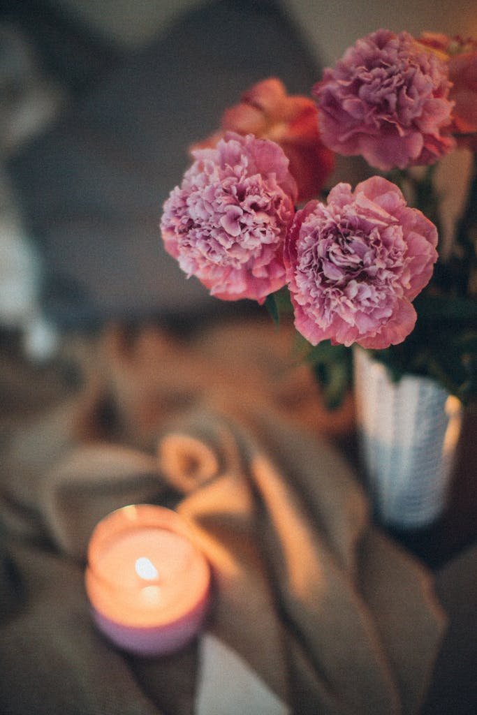 Delicate pink flowers in a vase alongside a glowing candle create a romantic ambiance.