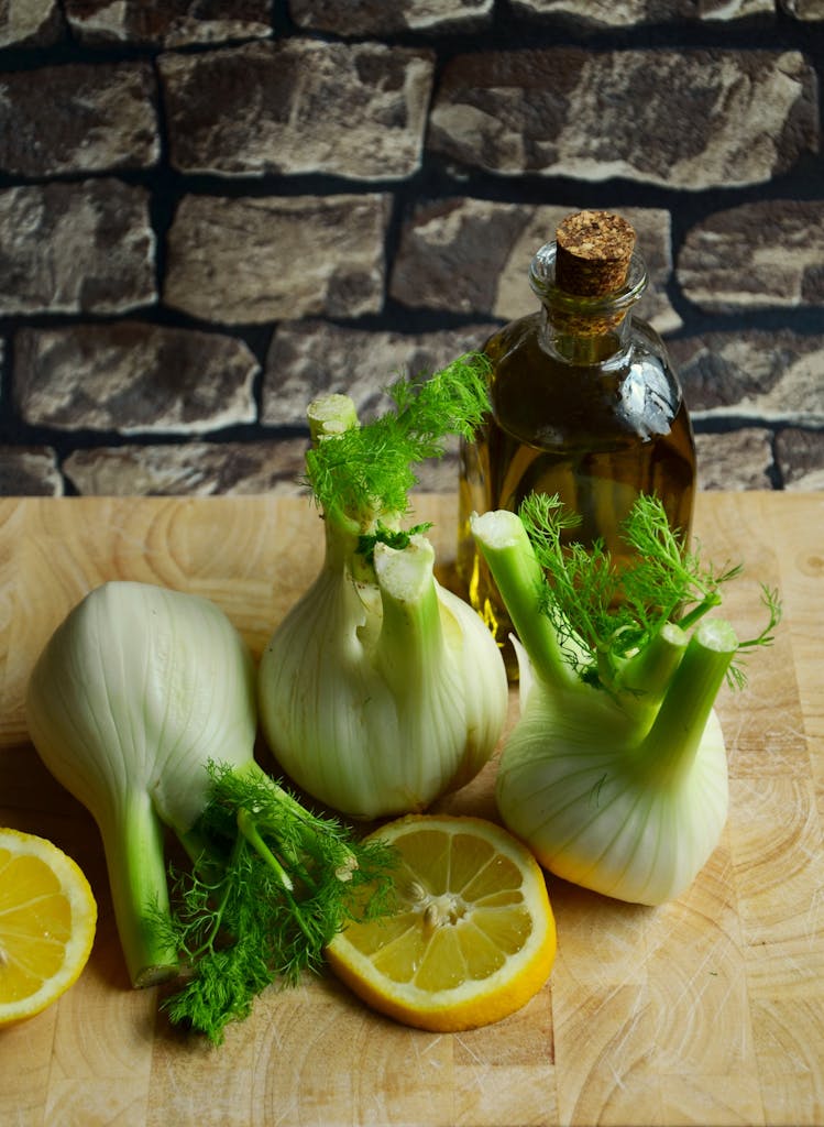 Fennel bulbs and lemon slices on a wooden table with olive oil, perfect for healthy cooking.