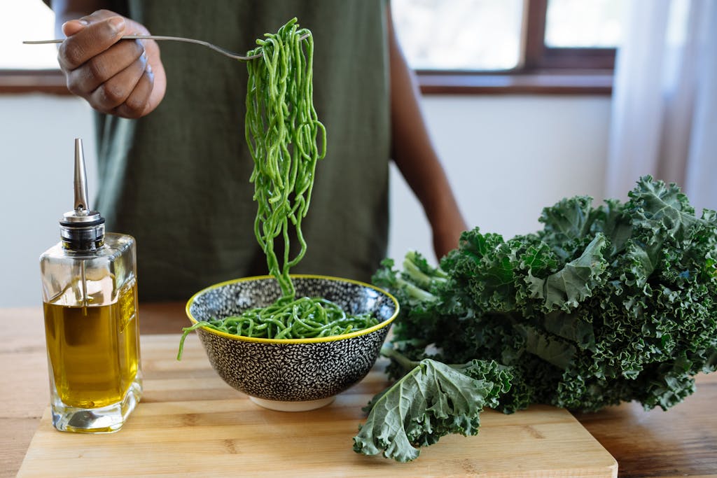 Fresh green kale noodles in a bowl with olive oil on a wooden table. Perfect for a healthy meal.