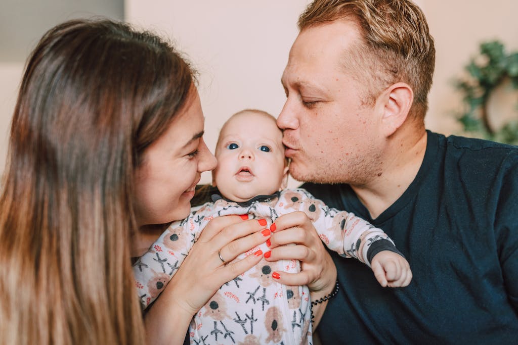 Loving parents embrace and kiss their newborn baby indoors.