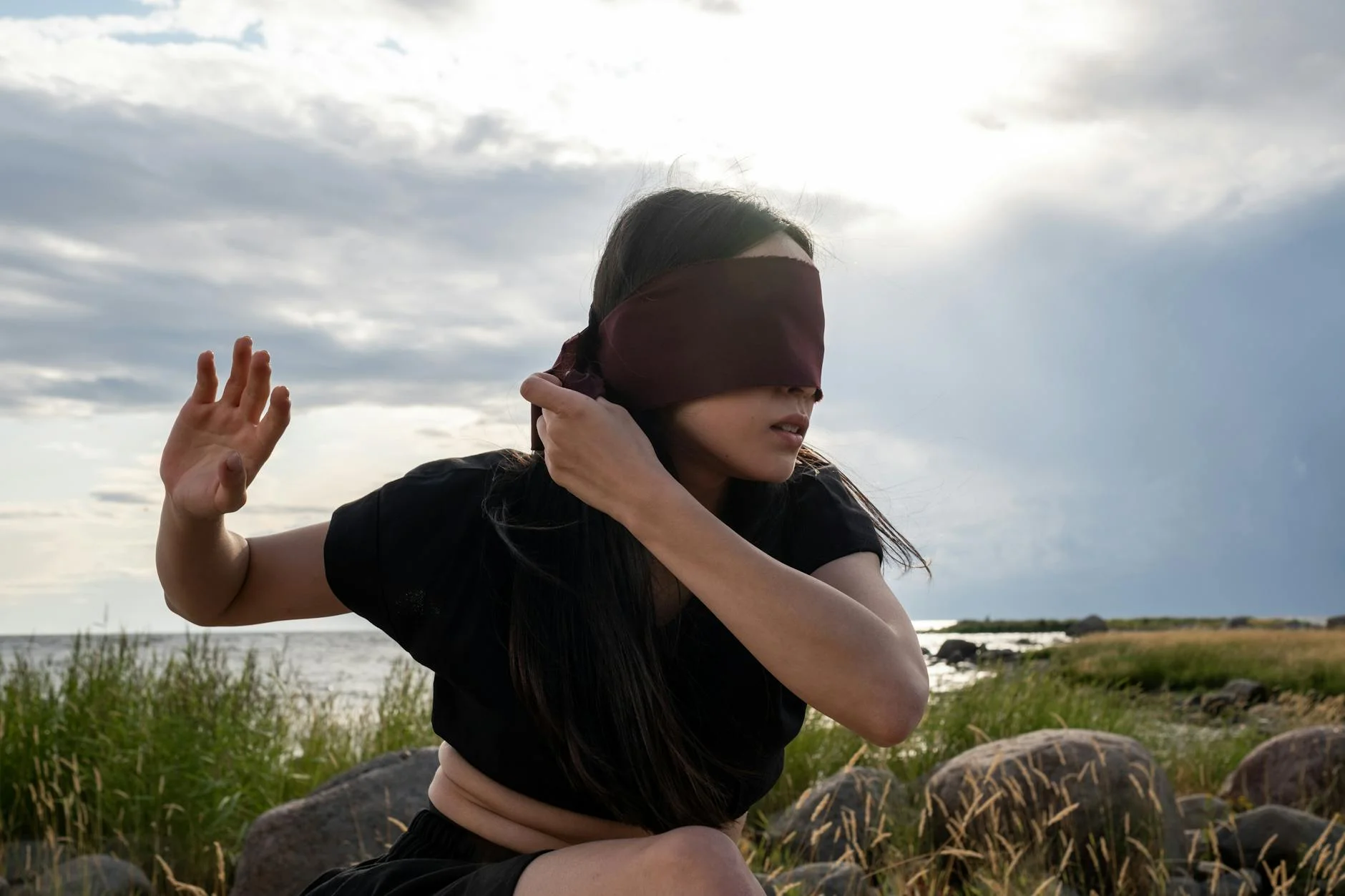 a woman in black crop top with blindfold sitting on rock