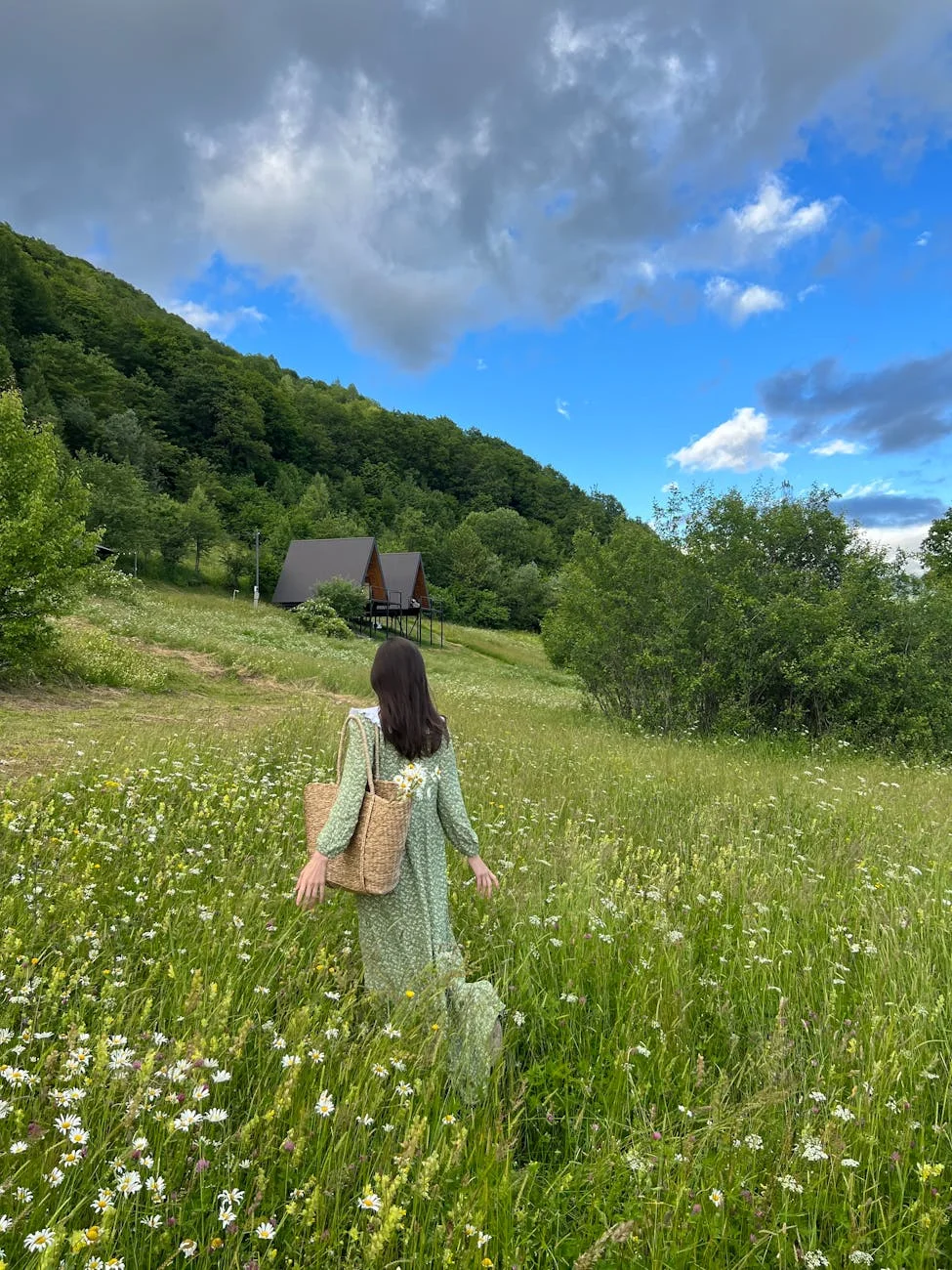 woman in green dress walking on meadow with flowers