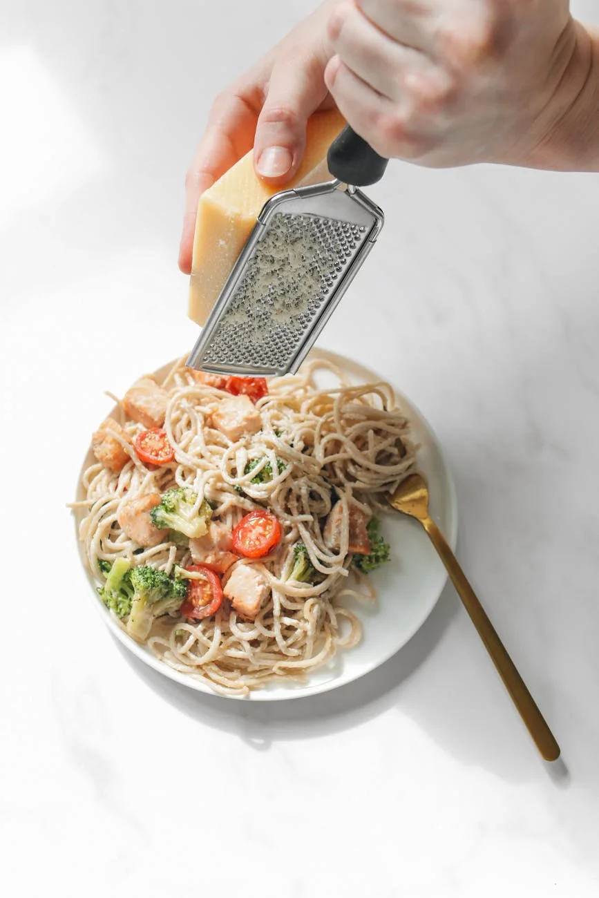 a person putting cheese on a pasta dish