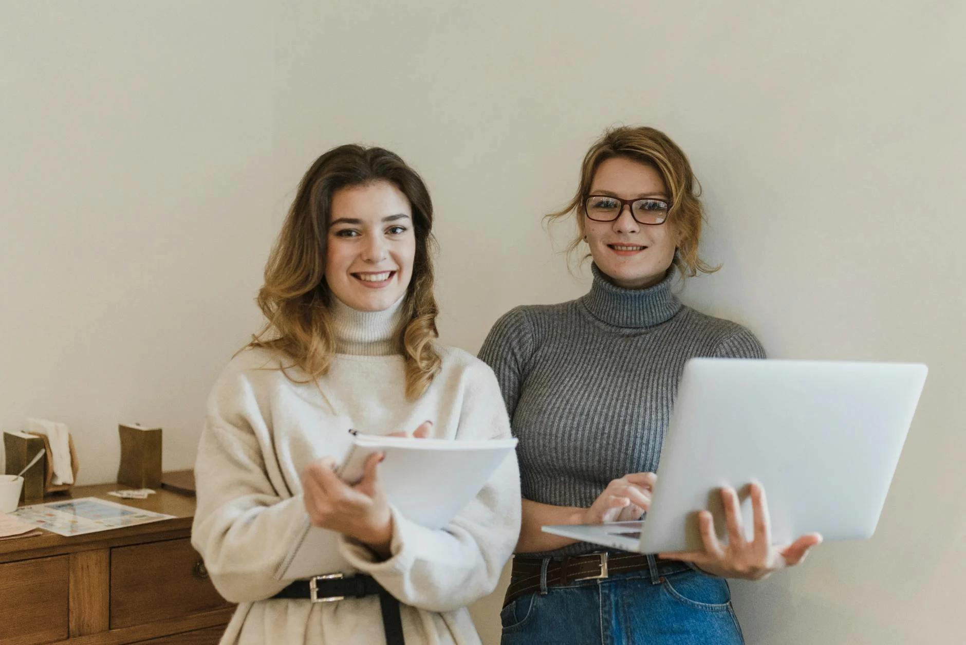 pretty women wearing turtlenecks holding a notebook and a laptop