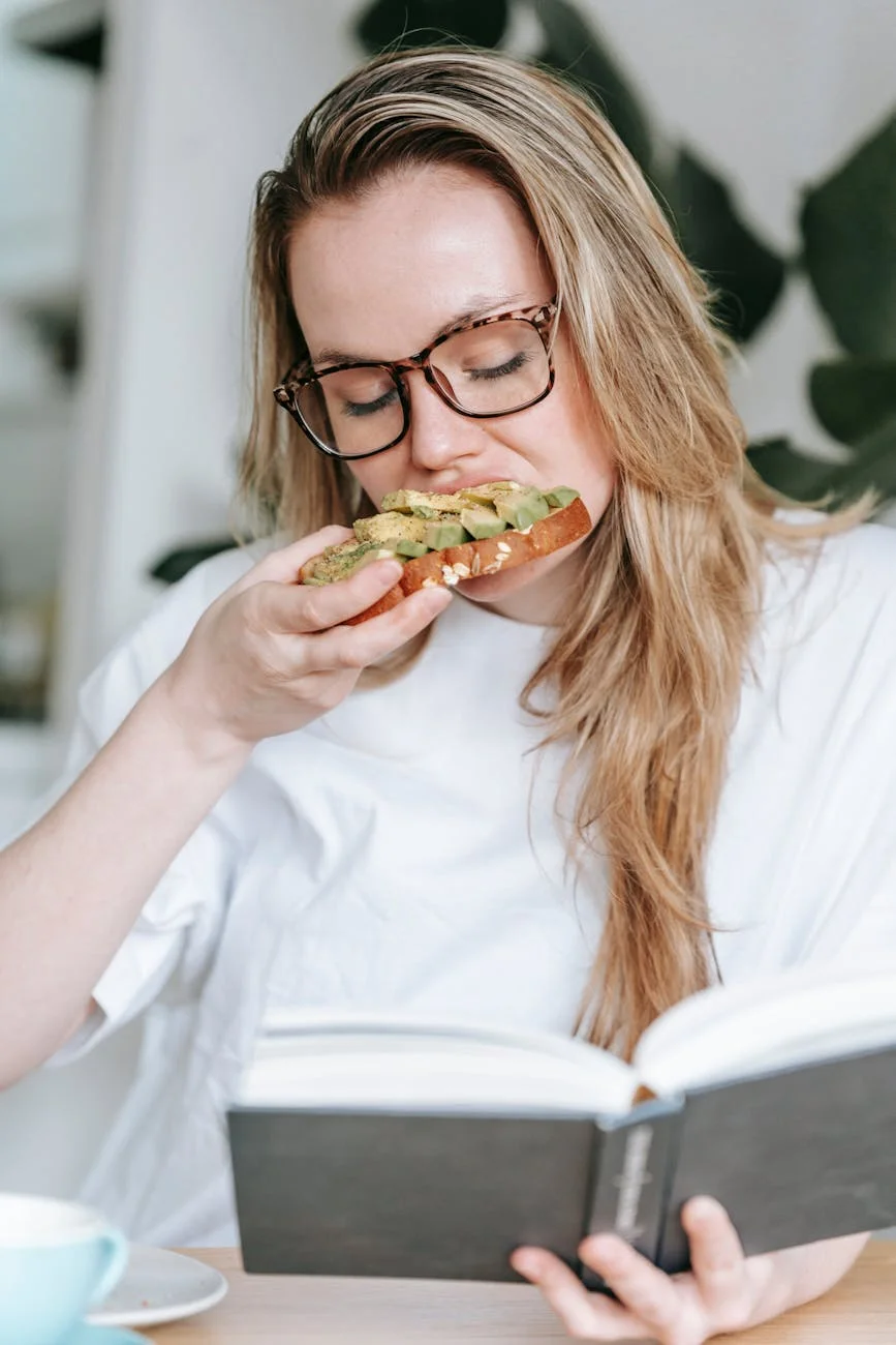 young woman eating sandwich while reading book