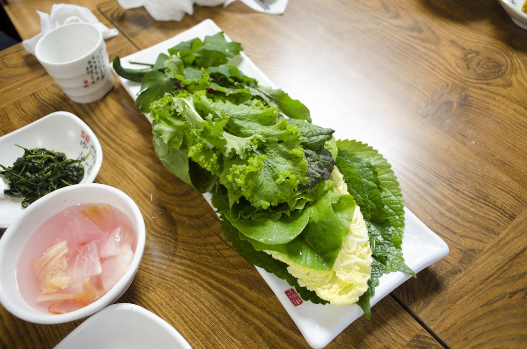 Platter of fresh leafy vegetables on a wooden table, ready for a healthy meal.