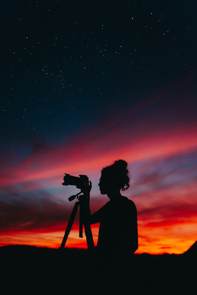 Silhouette of a photographer capturing the starry sky during a colorful sunset, creating a dramatic and artistic scene.