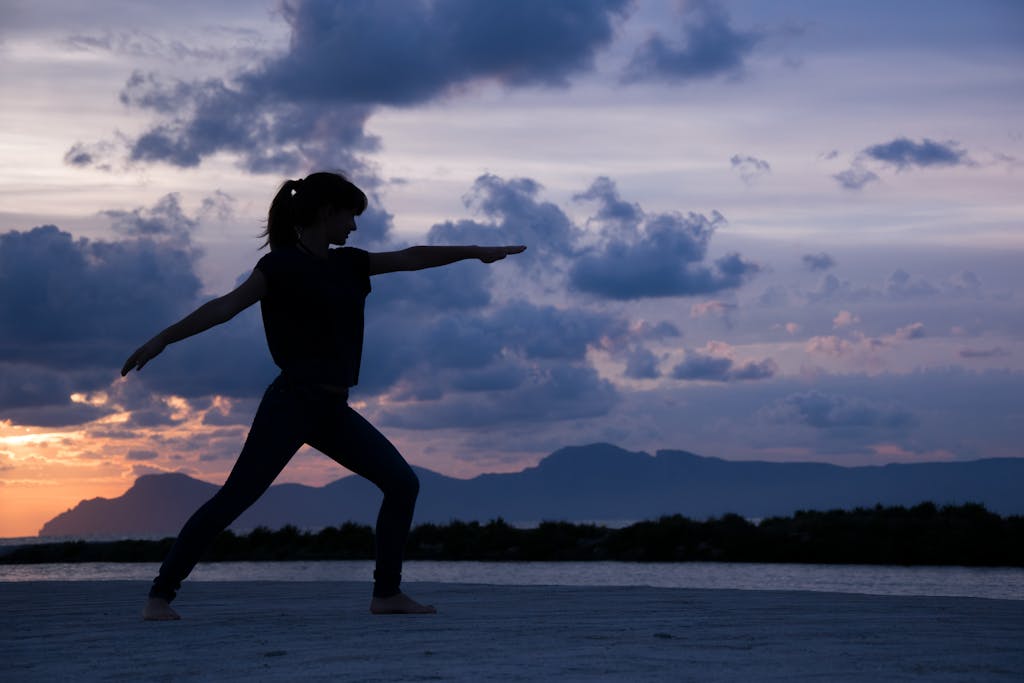 Silhouette of a woman practicing yoga at sunset with a dramatic cloudy sky backdrop.