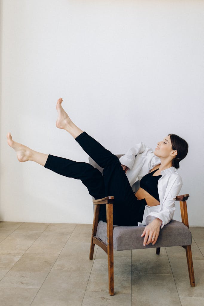 A barefoot woman in casual attire relaxing on a chair in a minimalist indoor setting.