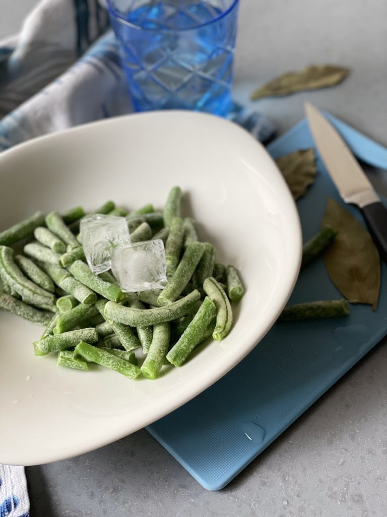 A bowl of frozen green beans with ice cubes, ready for meal prep.