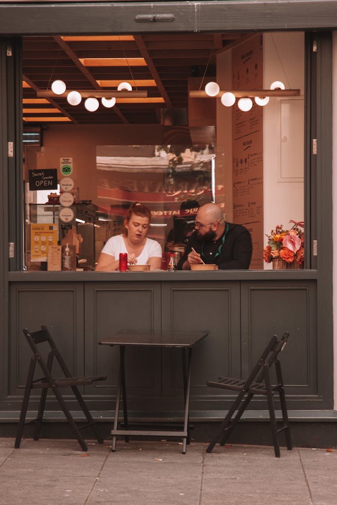 A candid shot of a man and woman gently conversing in a cozy cafe setting with a street view.