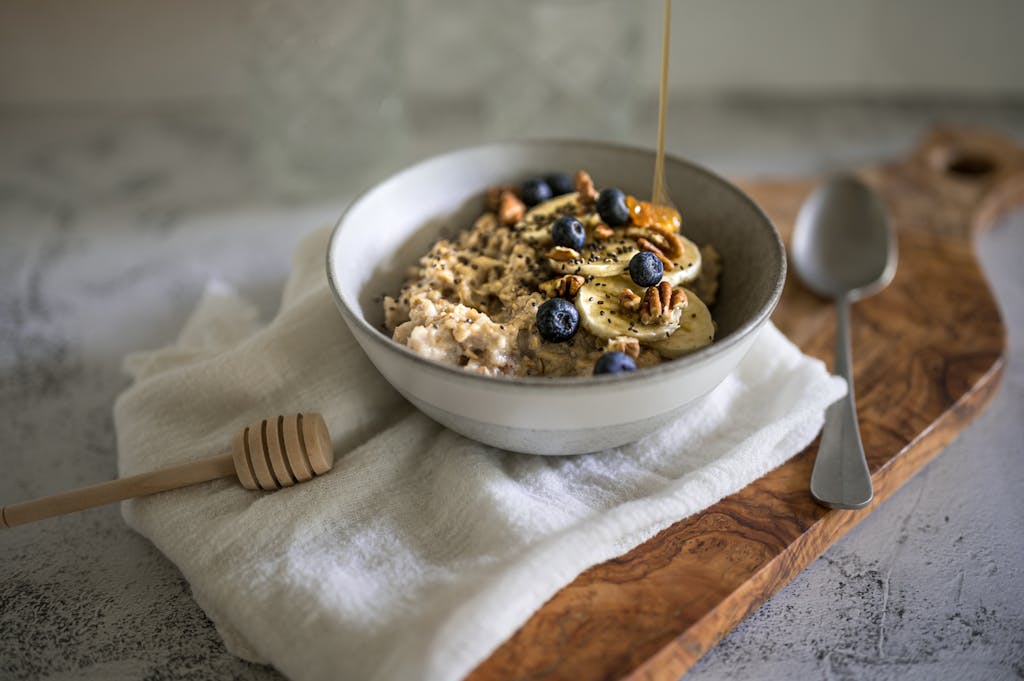 A ceramic bowl of oatmeal topped with blueberries, bananas, and walnuts on a wooden tray.