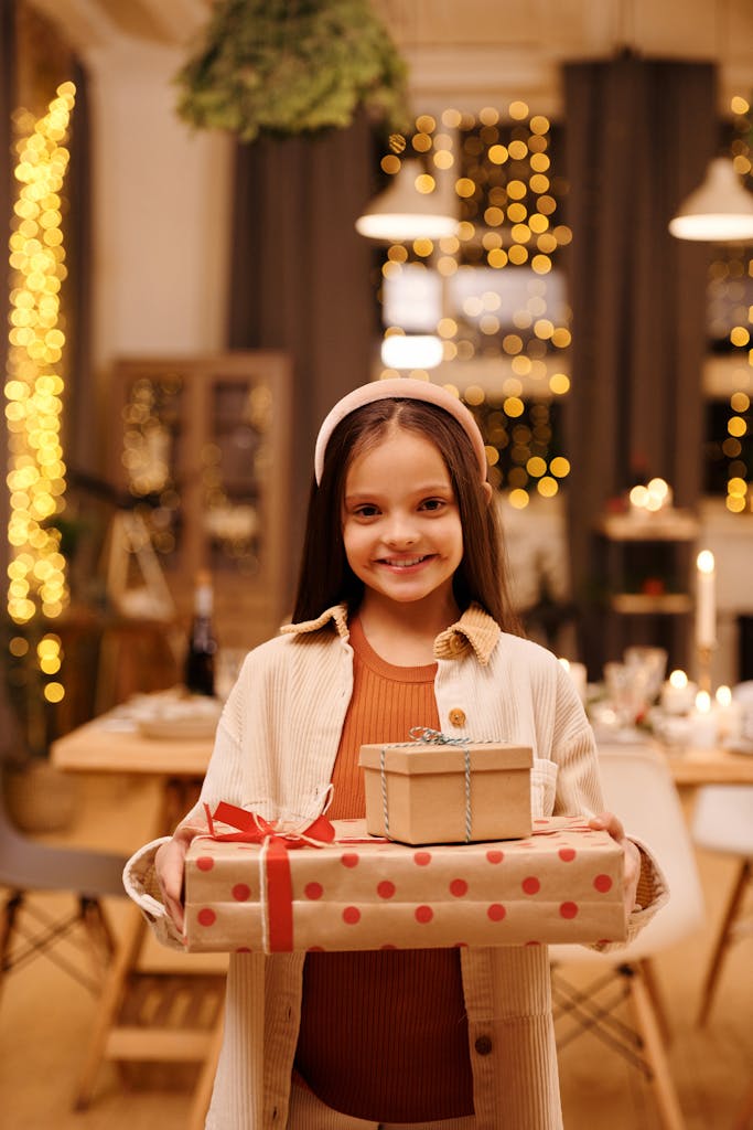 A cheerful young girl holding wrapped gifts in a festive holiday setting.
