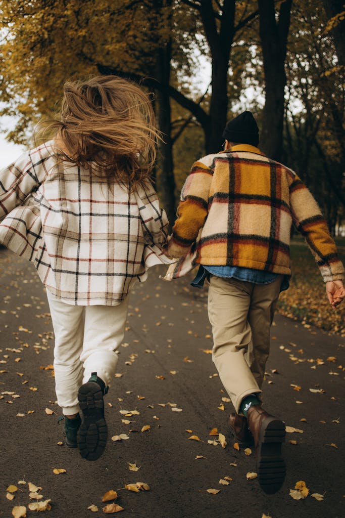 A couple in plaid jackets running on a leafy path in an autumn forest park.