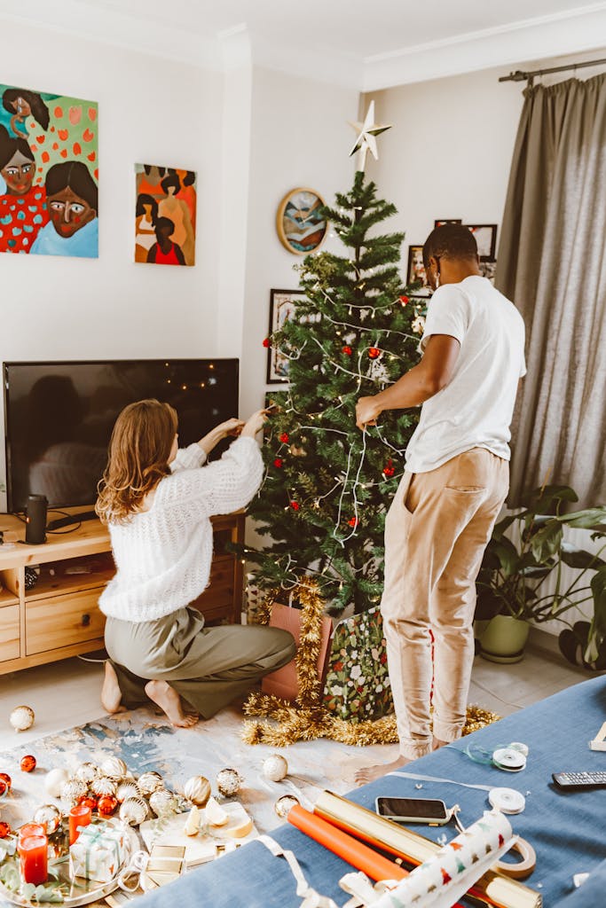 A couple joyfully decorating a Christmas tree in their living room, adding festive ornaments.