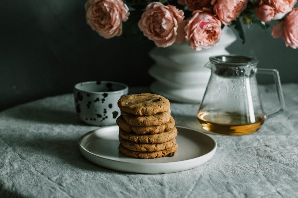 A cozy breakfast setup with cookies, tea, and pink roses on a table.