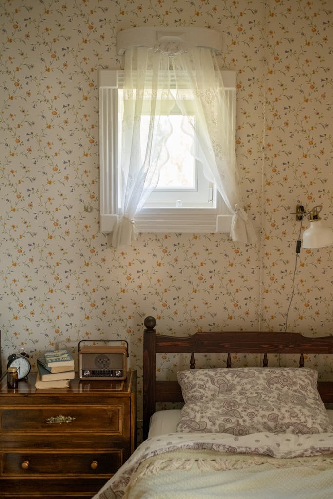 A cozy, vintage-style bedroom featuring a floral wallpaper, wooden bed, and nostalgic decor.