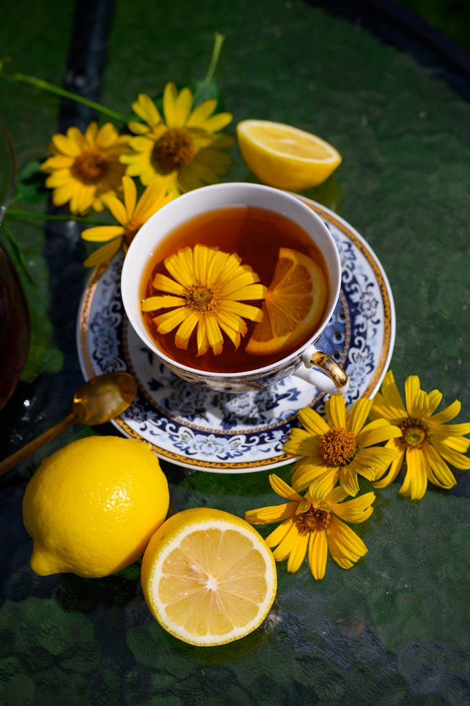 A cup of herbal tea with lemon slices and yellow flowers on a table, perfect for a refreshing morning.