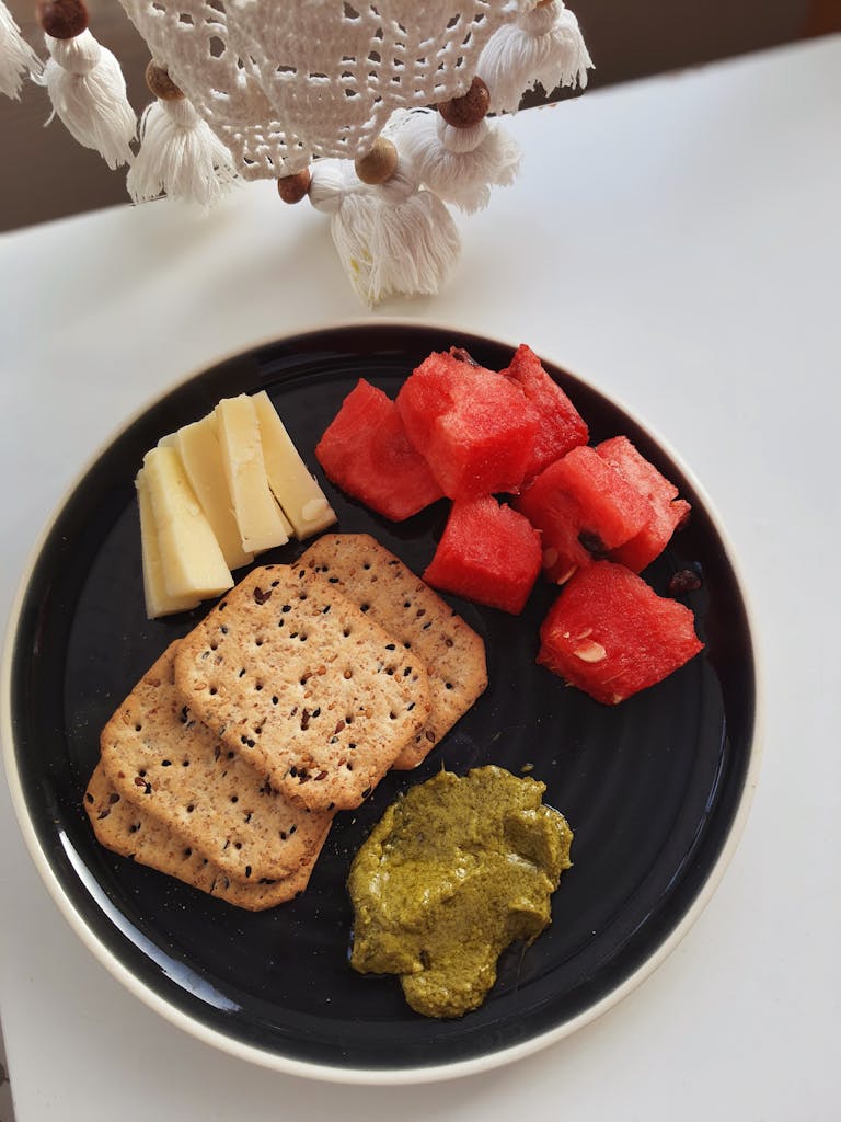 A delicious snack featuring cheese, watermelon, crackers, and pesto arranged on a plate.