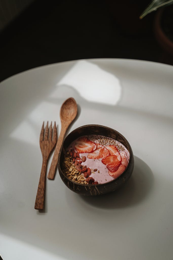A delicious strawberry smoothie bowl with seeds and oats in a wooden bowl on a white table.