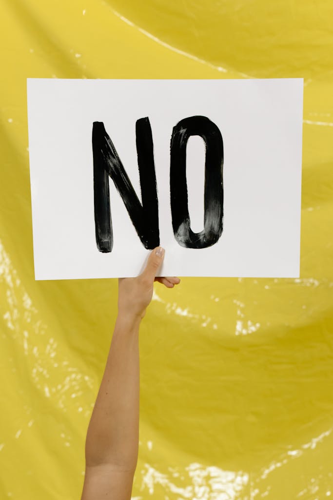 A hand holding a 'NO' sign against a bright yellow background.