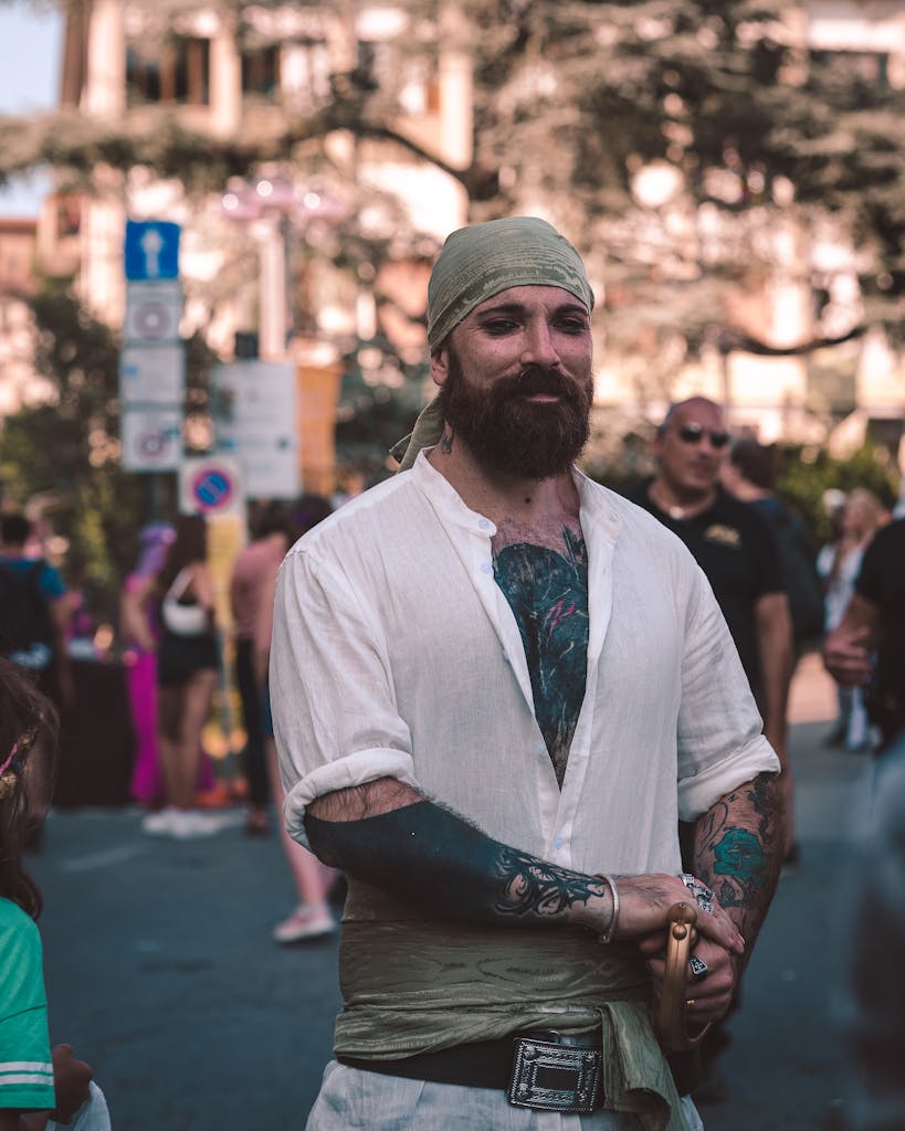 A man dressed as a pirate with tattoos and a bandana, posing outdoors.