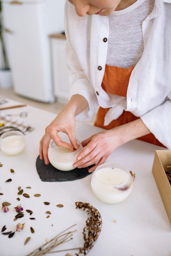 A person crafting handmade candles with dried flowers in a cozy indoor workspace.