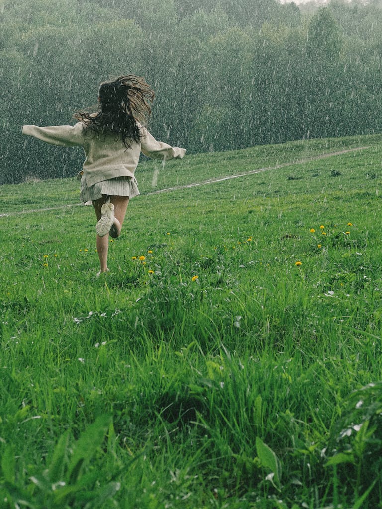 A person runs through a vibrant green field during a serene spring rain shower.