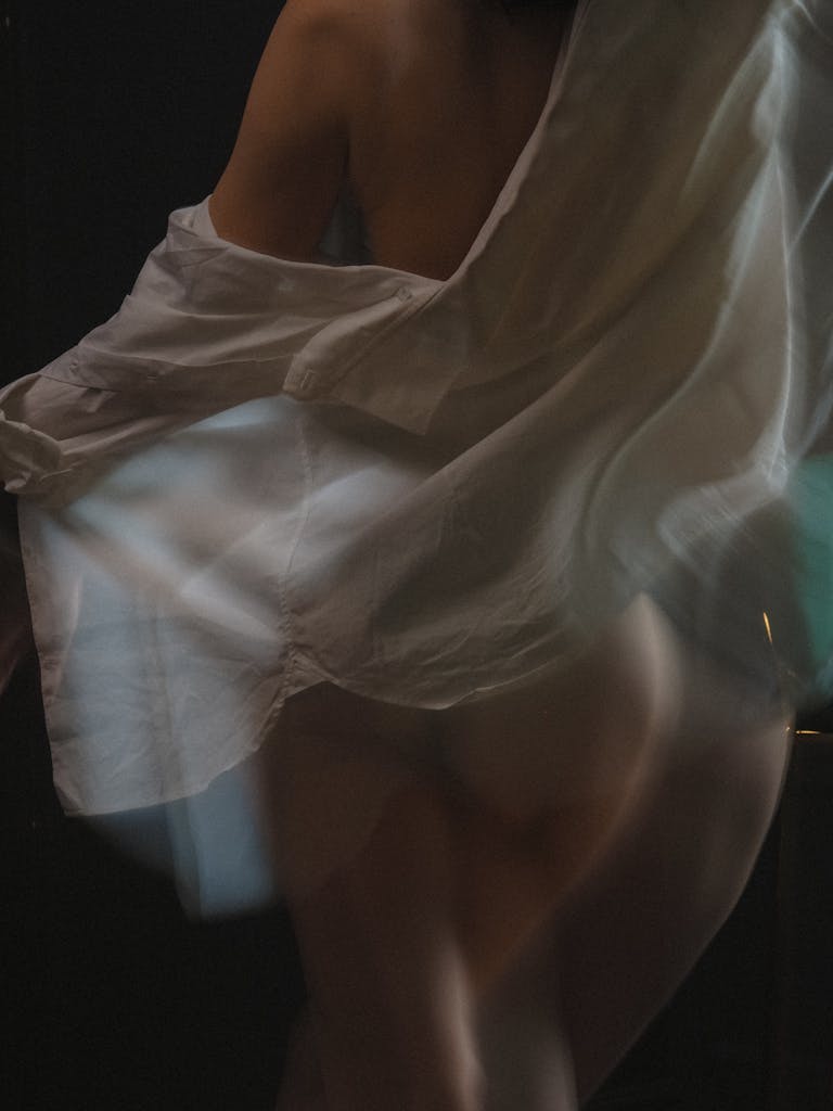 A sensual and artistic photo capturing motion blur of a woman draped in a white shirt.