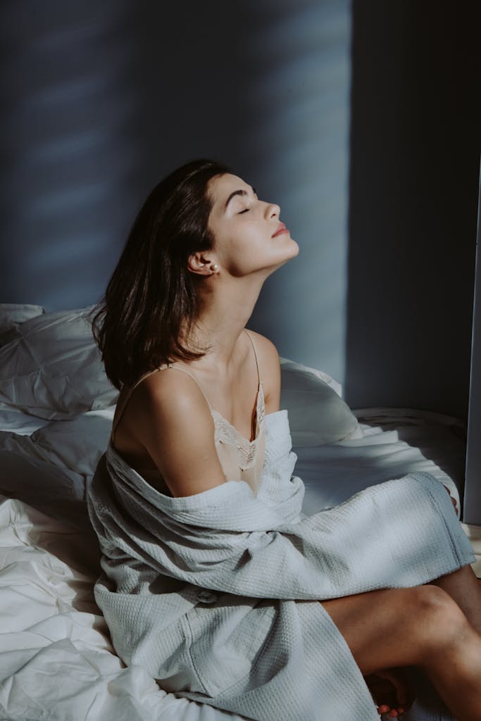 A serene moment of a woman sitting in a sunlit bedroom, embracing morning tranquility.
