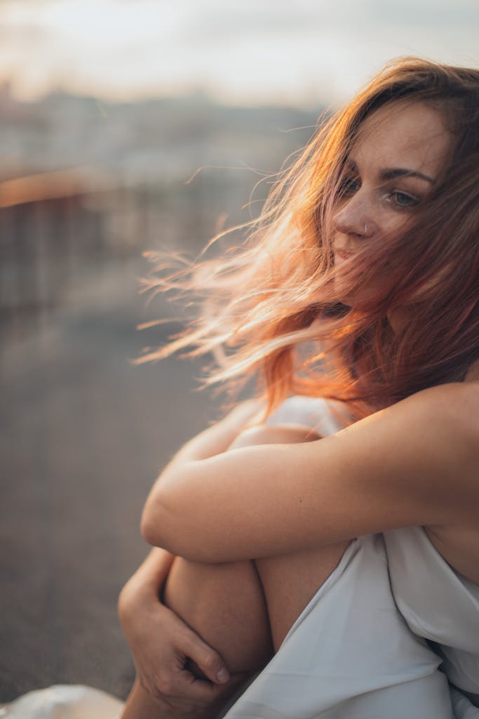 A serene portrait of a woman with flowing hair sitting outdoors at sunset, exuding tranquility.