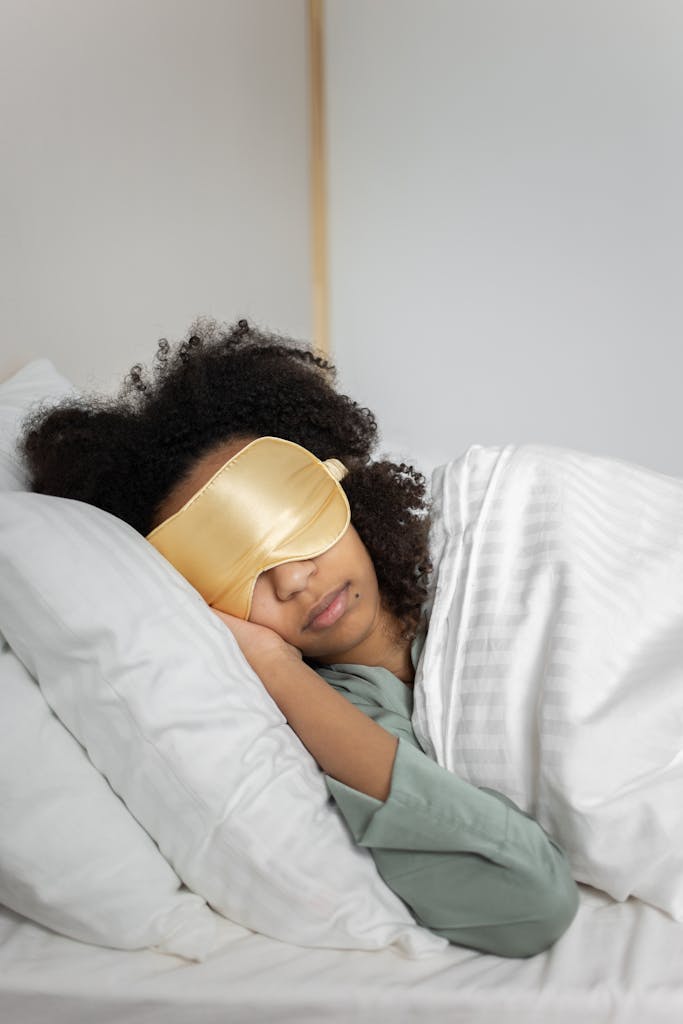 A serene scene of a black woman wearing a sleep mask, peacefully resting in bed.