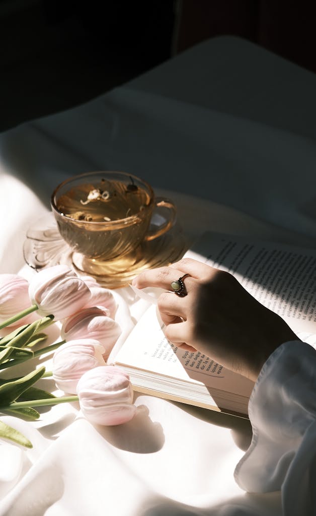 A serene scene of a hand reading a book next to tulips and a cup of coffee.