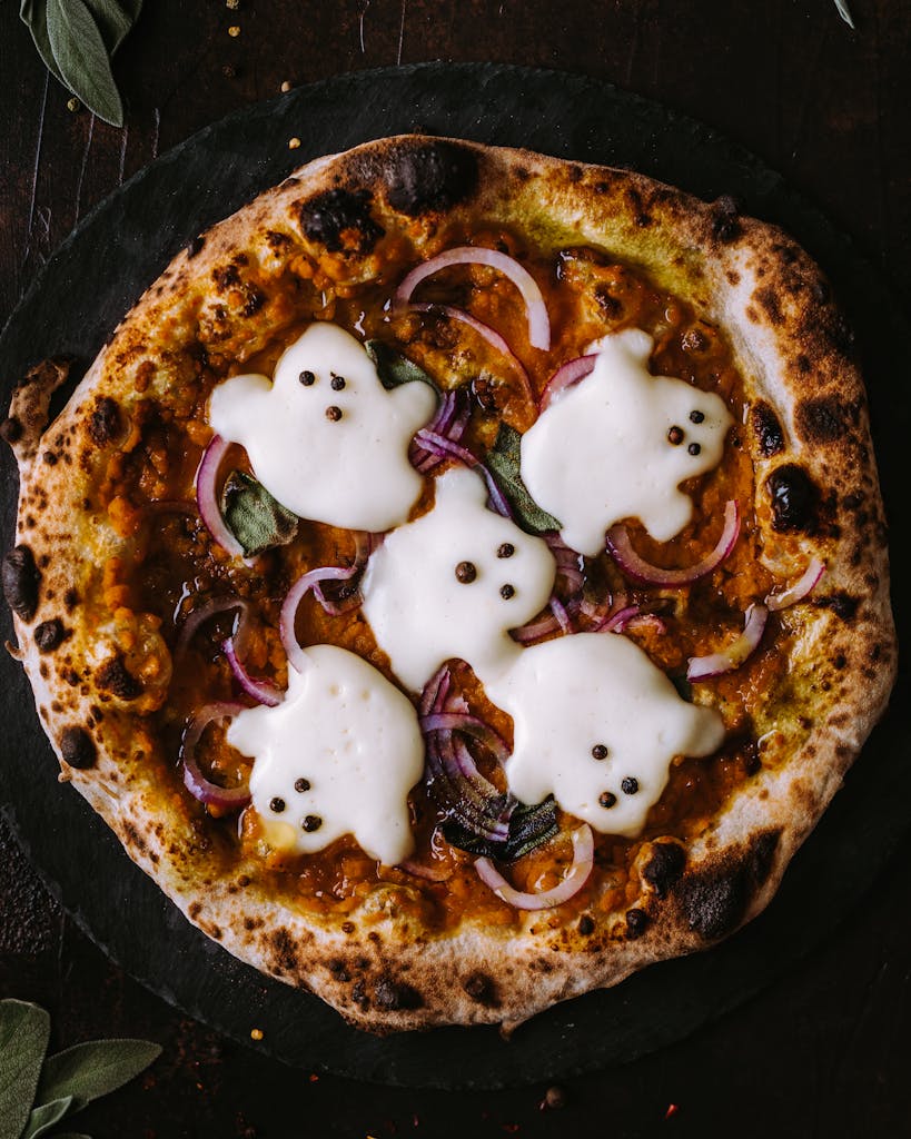 A spooky pizza decorated with ghost-shaped mozzarella, perfect for Halloween celebrations.