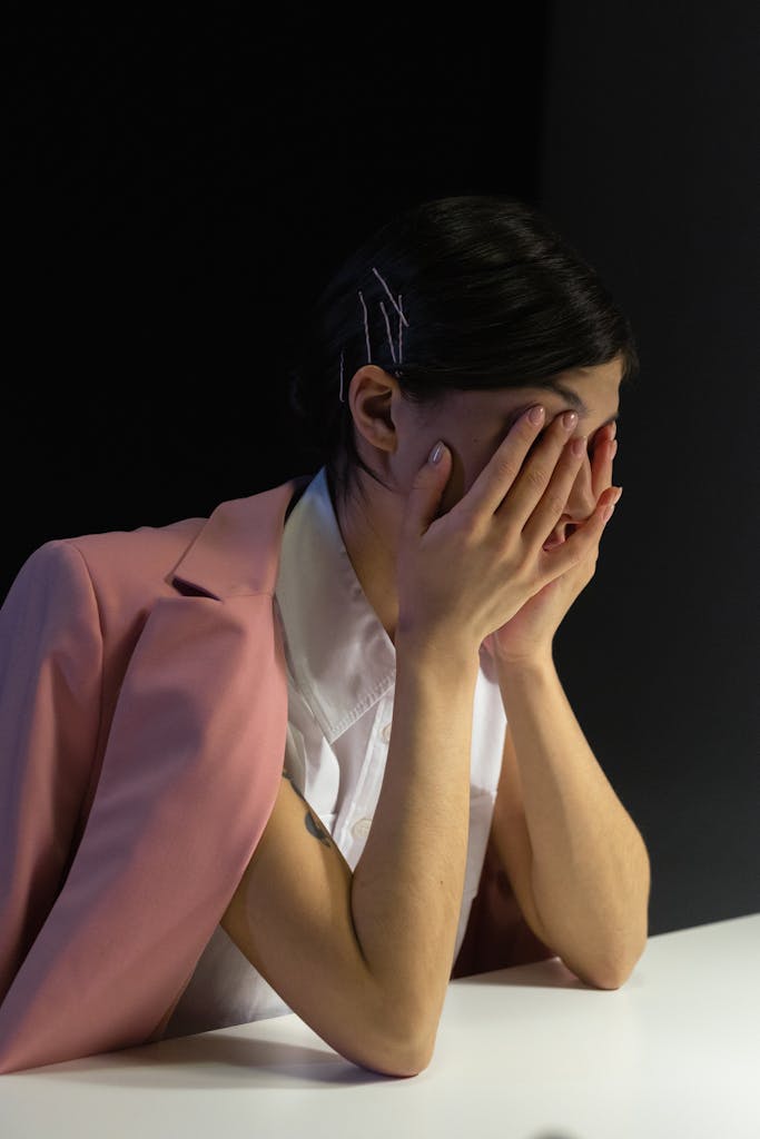 A stressed office worker in a pink jacket covering face, showcasing workplace fatigue.