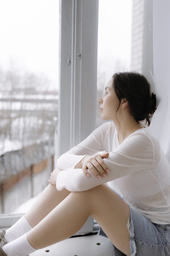 A thoughtful woman looks out a window, reflecting during winter.