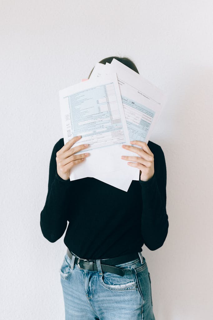 A woman concealing her face with tax forms, illustrating financial stress and paperwork burden.