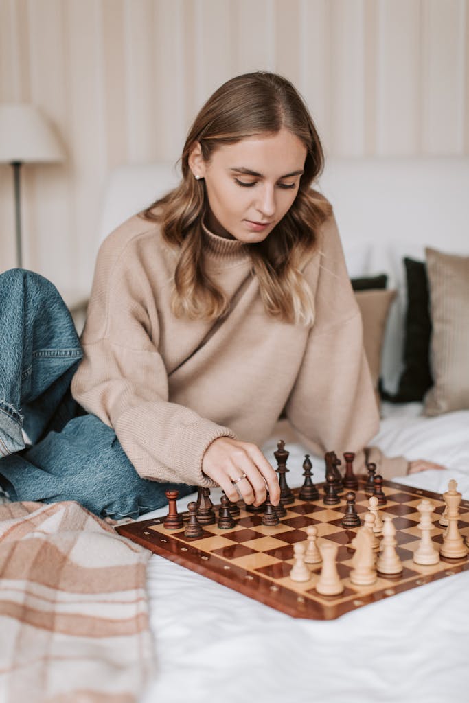 A woman concentrates on a chess game in a cozy bedroom setting.