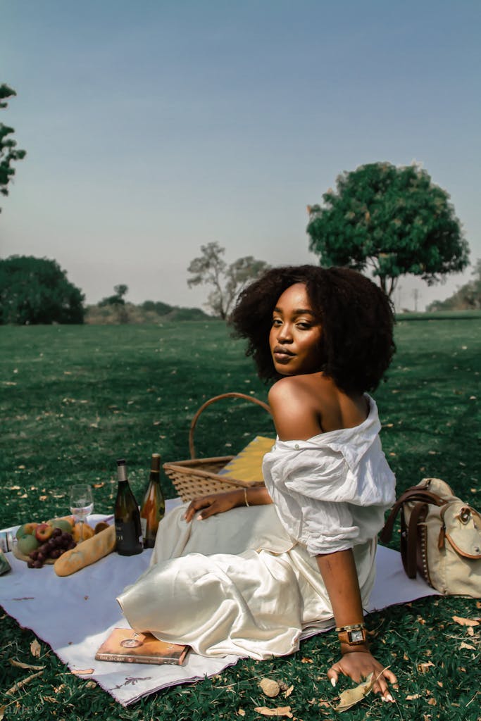 A woman enjoys a serene picnic on a sunny day with wine and fruit.