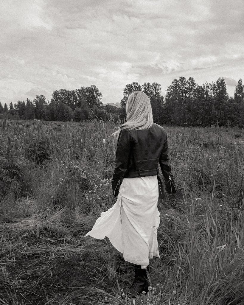 A woman in a white dress walks through a meadow in a moody black and white setting.