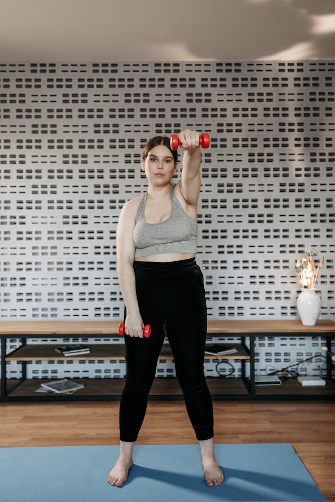 A woman in activewear lifting dumbbells indoors for a healthy lifestyle.