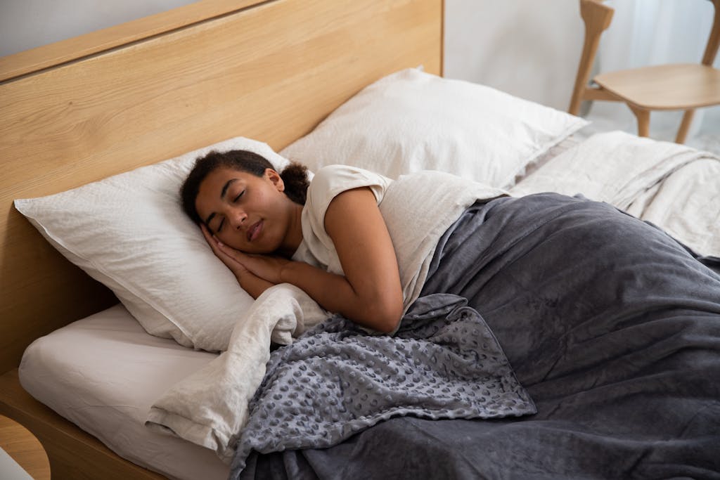 A woman peacefully sleeping in bed using a cozy weighted blanket, promoting relaxation.