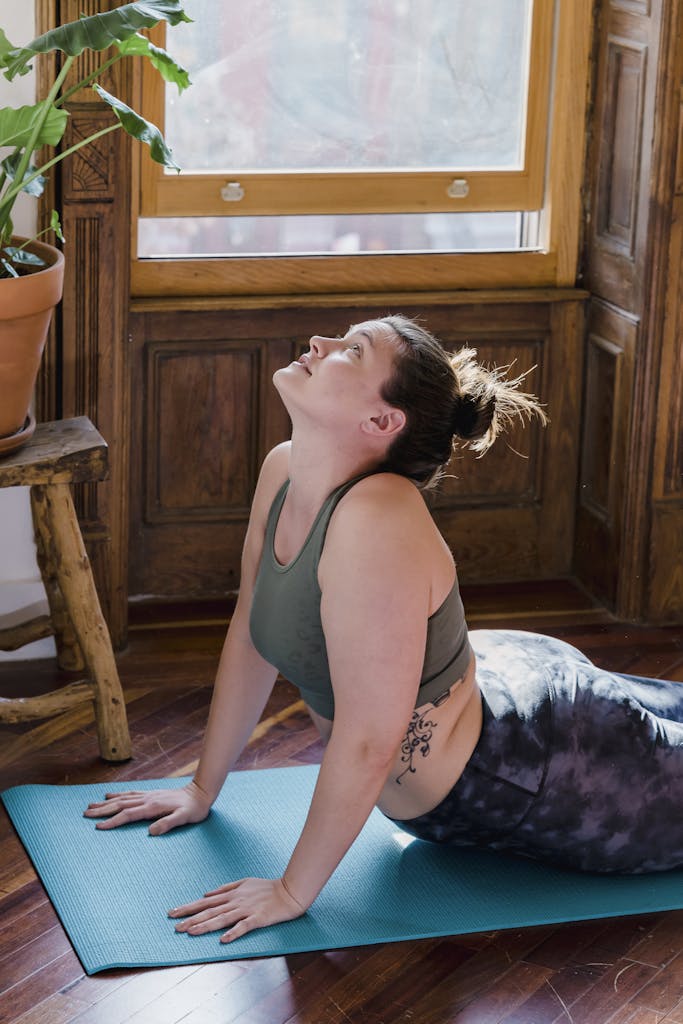 A woman performing a yoga pose on a mat indoors, bathed in morning sunlight.