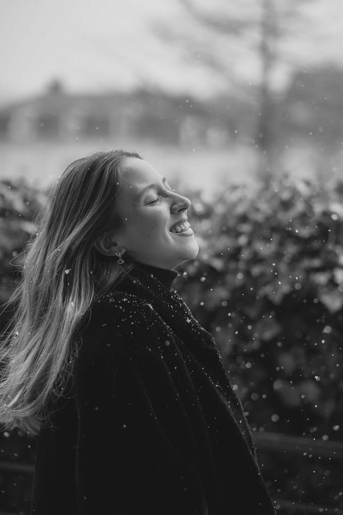 A woman smiling with joy as snowflakes fall in a serene winter setting.