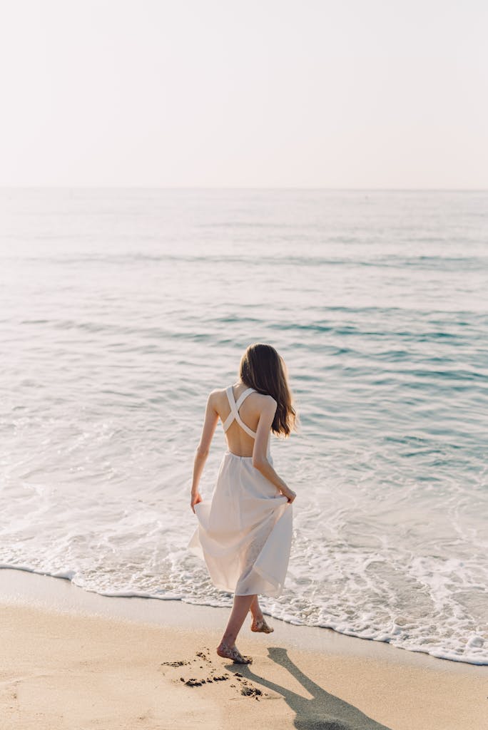 A woman walks barefoot on a sandy beach, enjoying a serene summer day by the sea.