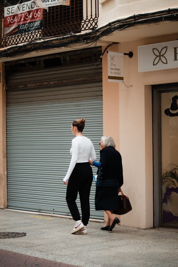 A young woman assists an elderly lady walking down a street in Valencia, Spain.